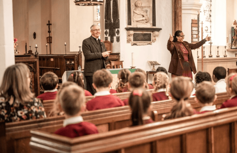 A group of school children visit a church, with someone signing from the front.