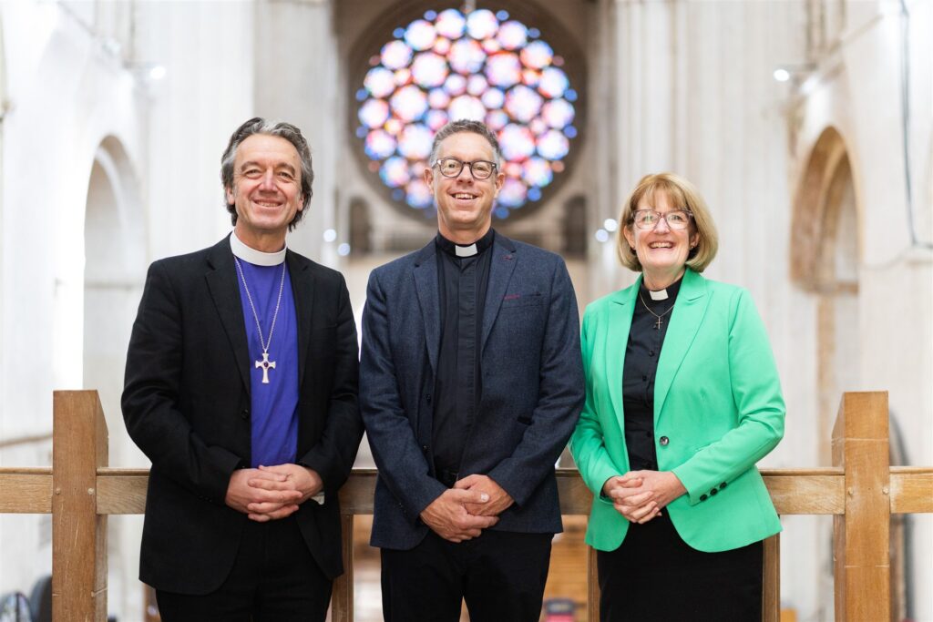 Bishop Andrew Rumsey, Tim Lomax, and Dean Jo Kelly-Moore pictured in front of the Rose Window at St Albans Cathedral